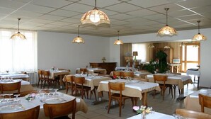 A dining area with multiple tables and chairs, ceiling lights, and a window with curtains. - Hôtel du Marché (Beauvoir-sur-Mer)