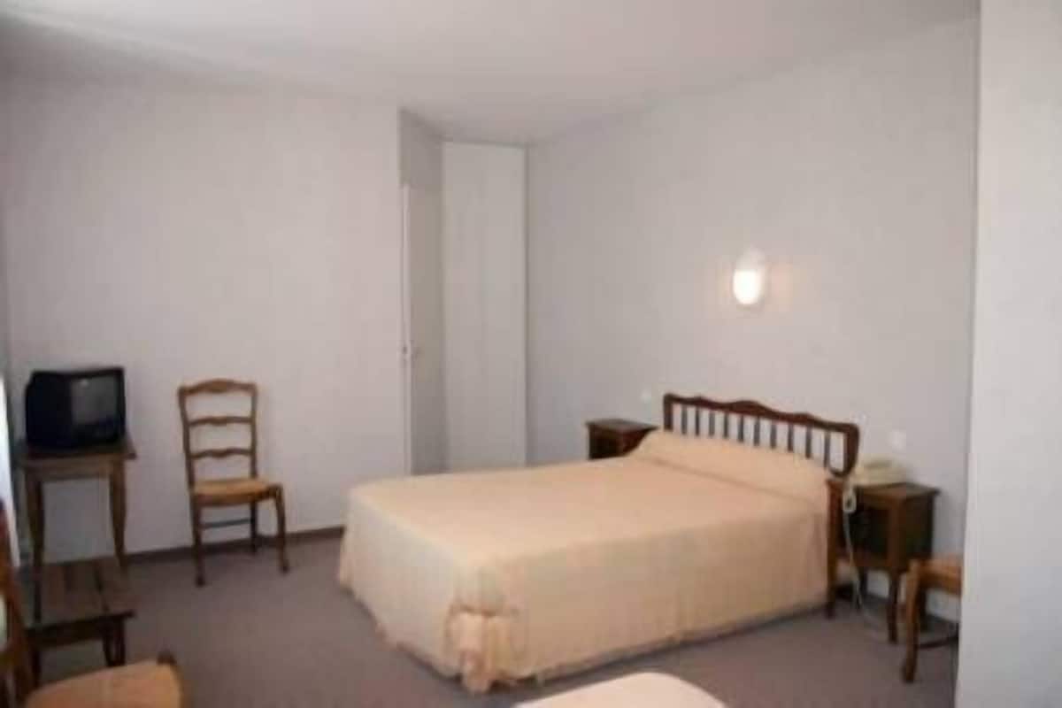 A small, simple room with a single bed, a chair, a table, and a television.