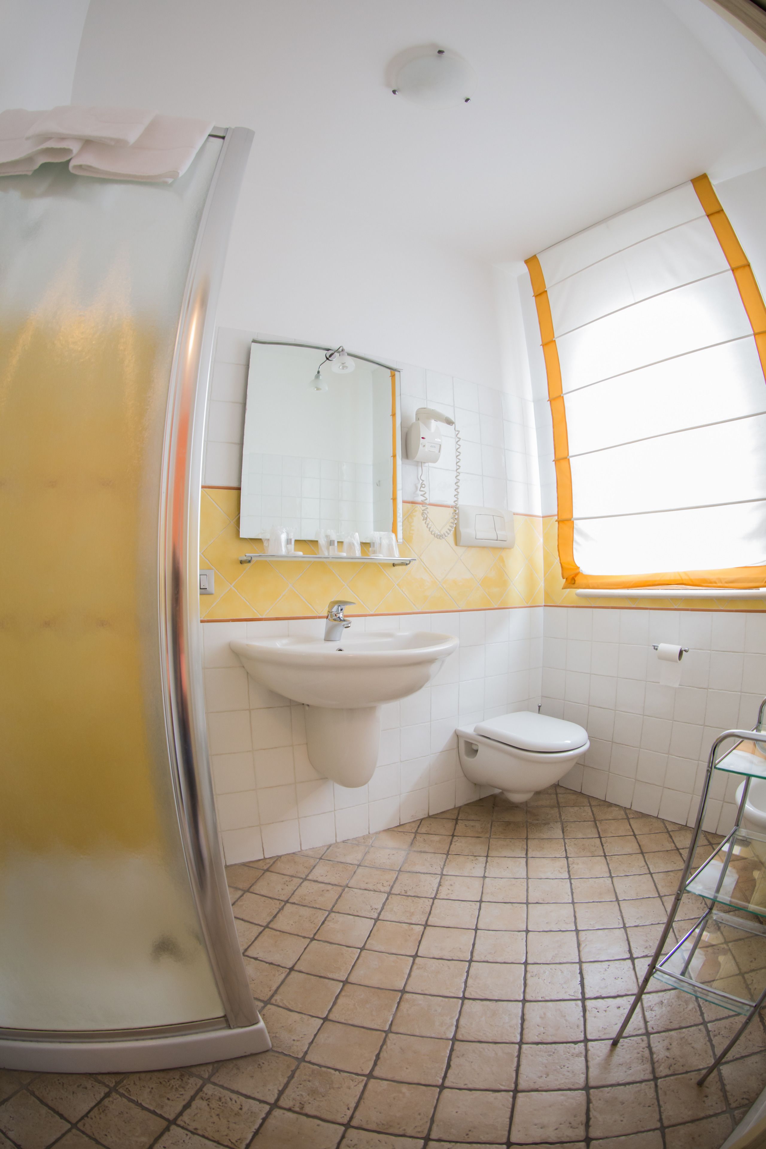 Ein Badezimmer mit Dusche, Waschbecken, Toilette und einem Fenster mit orangefarbenen Vorhängen.