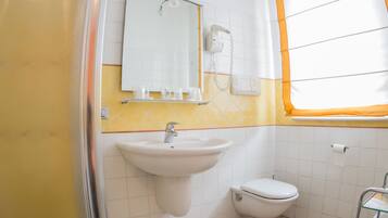 Ein Badezimmer mit Dusche, Waschbecken, Toilette und einem Fenster mit orangefarbenen Vorhängen.