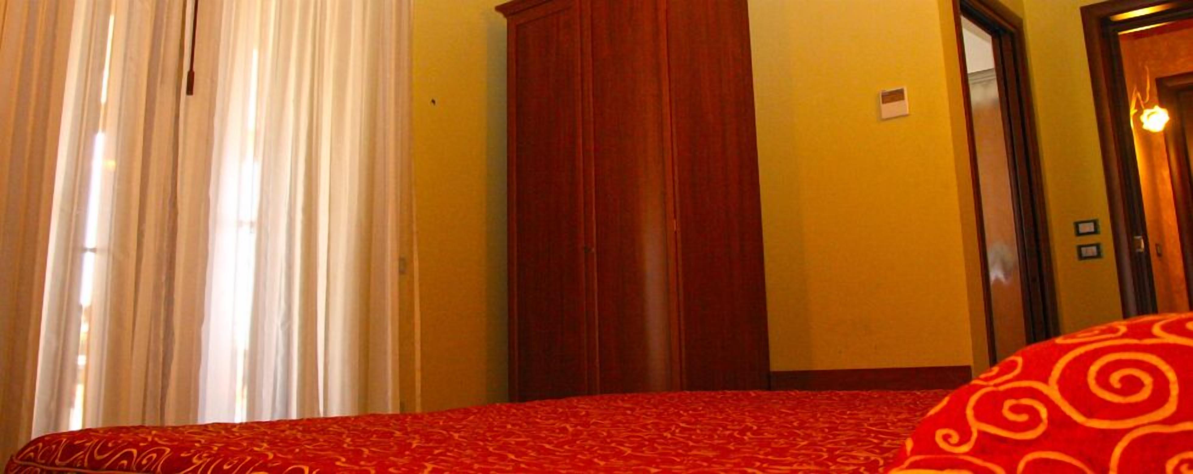 A hotel room with a bed, a wooden wardrobe, and a door.