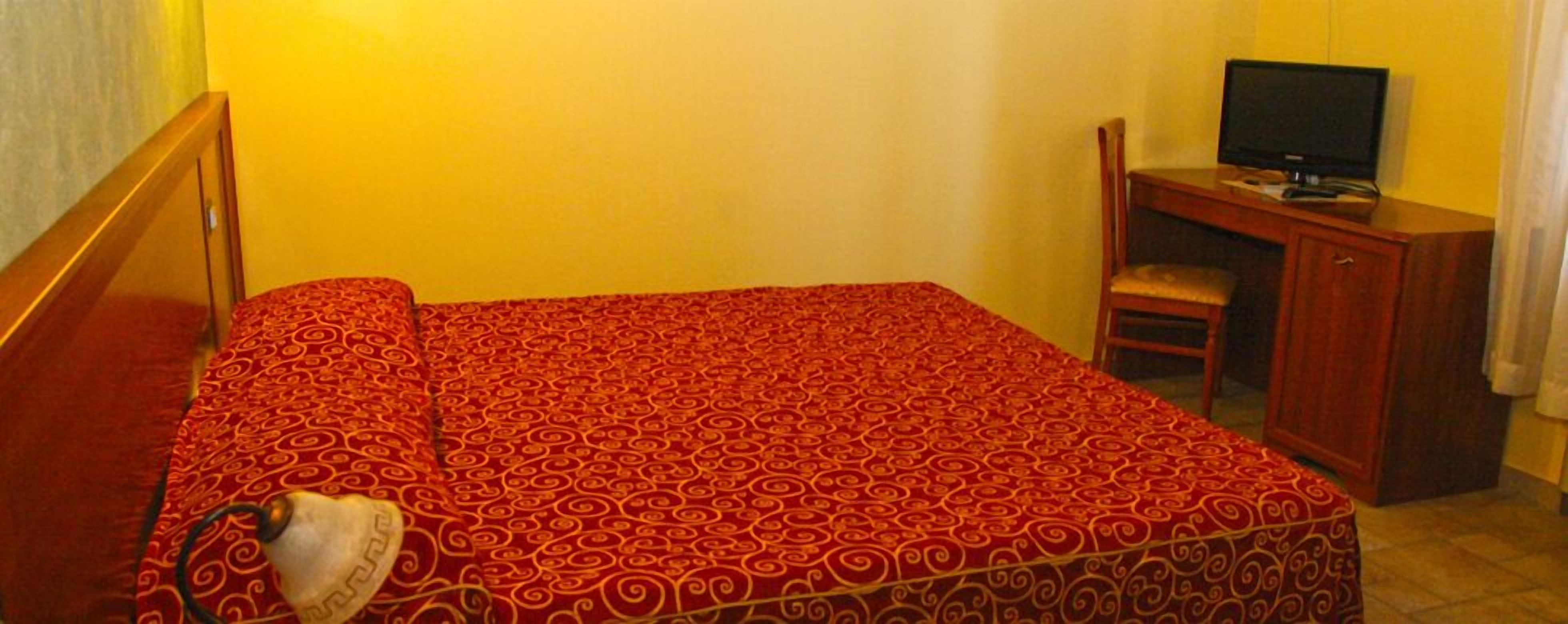 A hotel room with a bed, a desk, a chair, and a television.