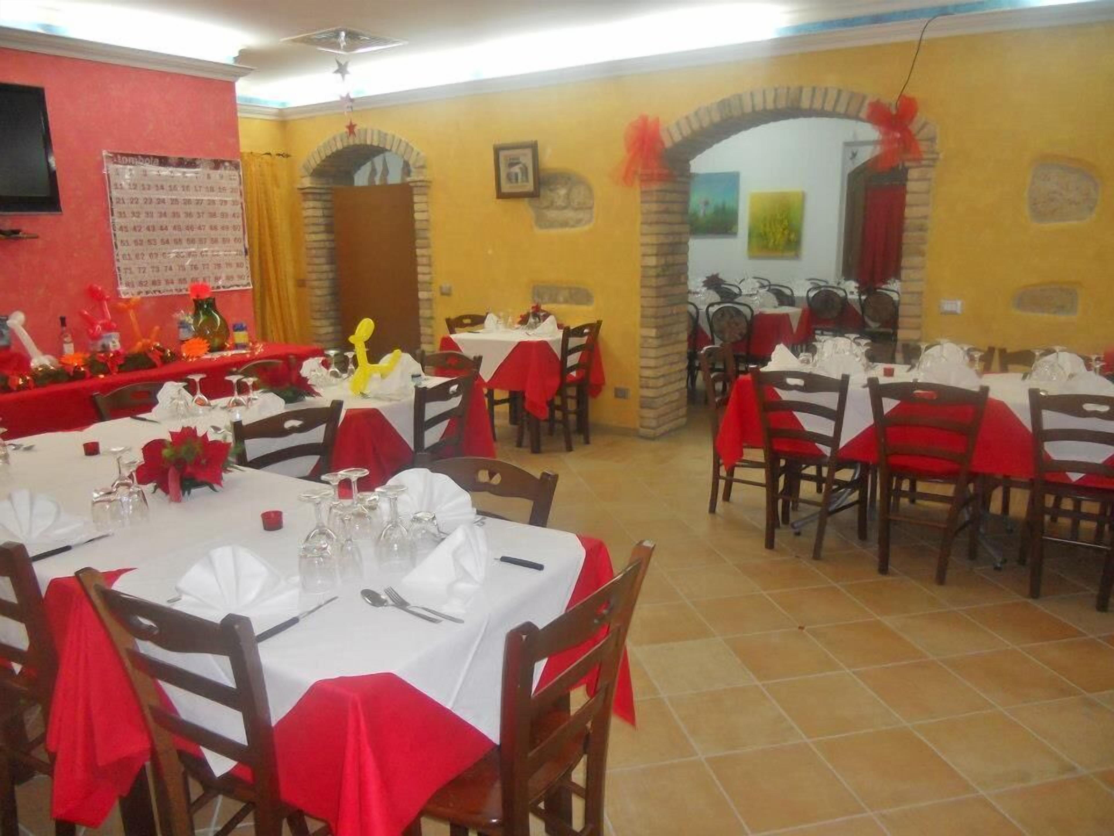 A dining area with tables set for a meal, featuring red tablecloths and wooden chairs.