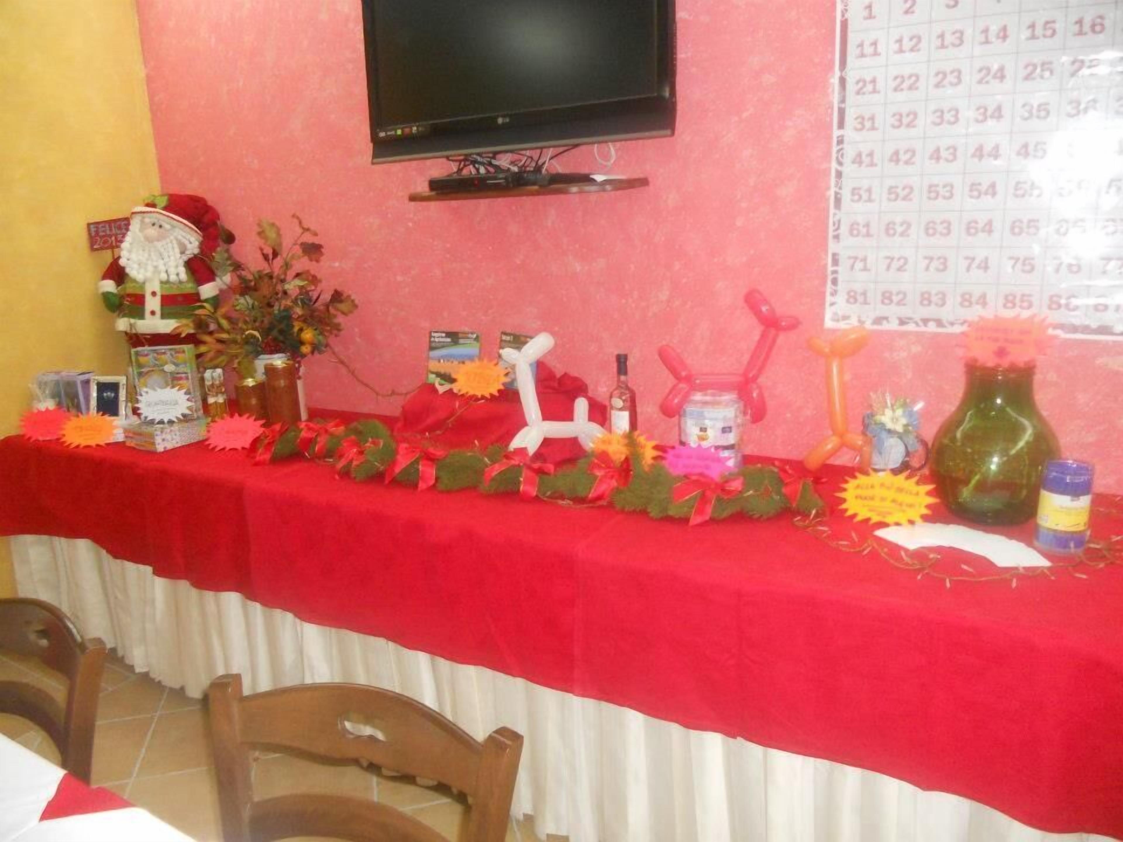 A decorated table with a red tablecloth, a television mounted on the wall, and various items including a Santa Claus figure, a bottle, and a vase.