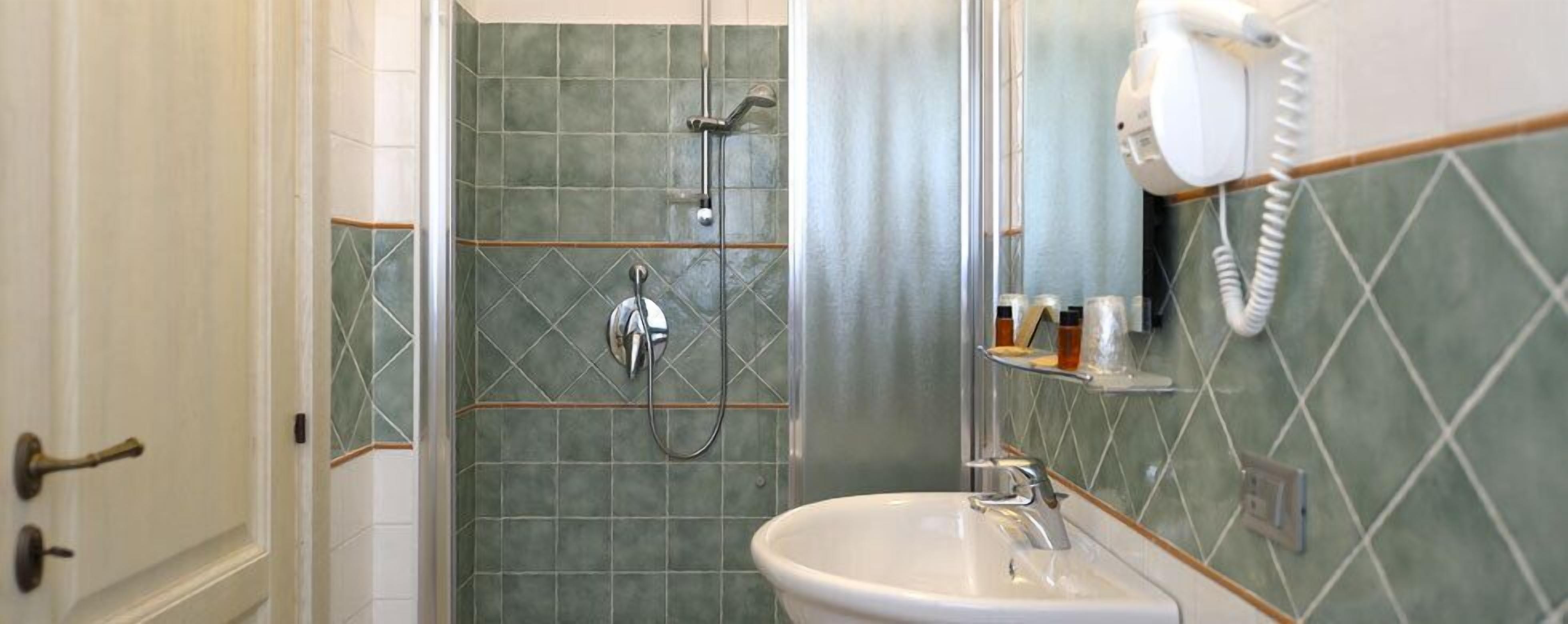 A bathroom with a shower, a sink, and a hairdryer mounted on the wall.