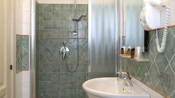 Un baño con ducha, lavamanos y un secador de pelo fijado a la pared.