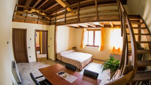 A room with a wooden ceiling, a bed, a table with chairs, and a staircase. - Il Vecchio Mulino (Chieti)
