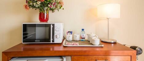 A hotel room with a microwave, a small table with a vase of flowers, a lamp, and a coffee maker.