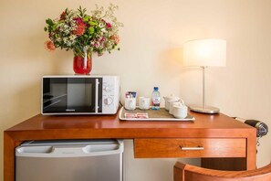 A hotel room with a microwave, a small table with a vase of flowers, a lamp, and a coffee maker. - Kathu Inn (Kathu)