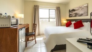 A hotel room with a bed, a desk with a microwave, a chair, a TV, and a window with curtains. - Kathu Inn (Kathu)