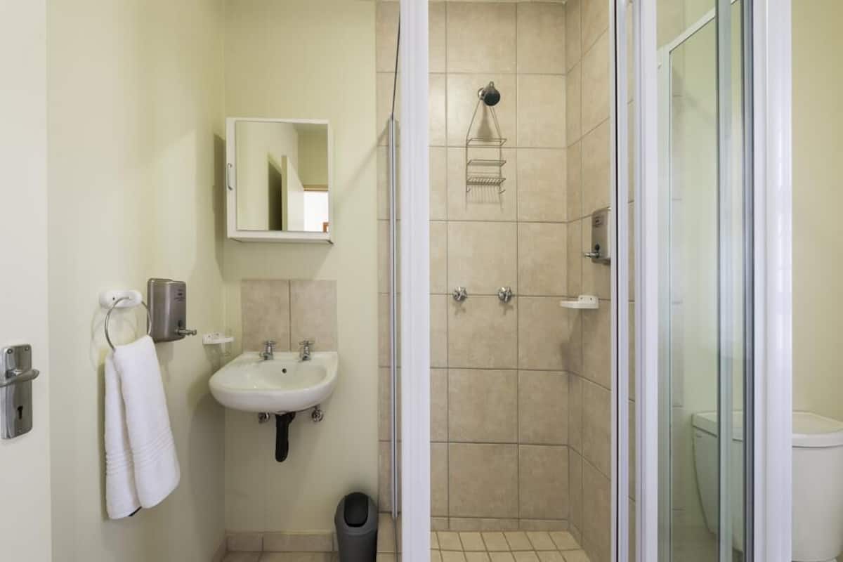 A bathroom with a sink, mirror, towel rack, and shower area.