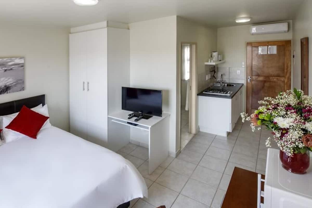 A hotel room with a bed, a TV, a desk, a kitchenette, and a bathroom.