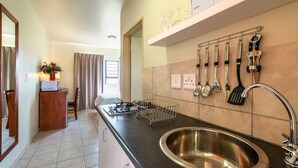 A modern kitchen with a stainless steel sink, a black countertop, and a variety of kitchen utensils hanging on the wall. - Kathu Inn (Kathu)