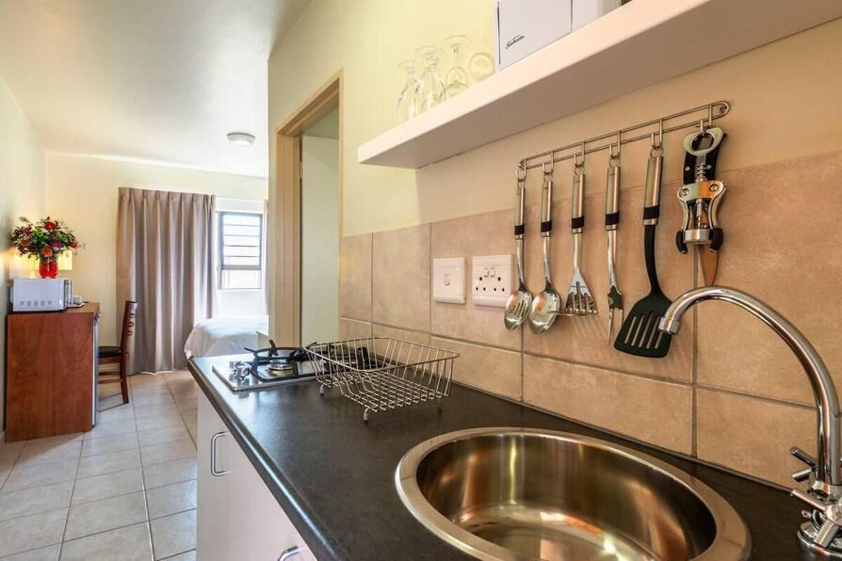 A modern kitchen with a stainless steel sink, a black countertop, and a variety of kitchen utensils hanging on the wall.