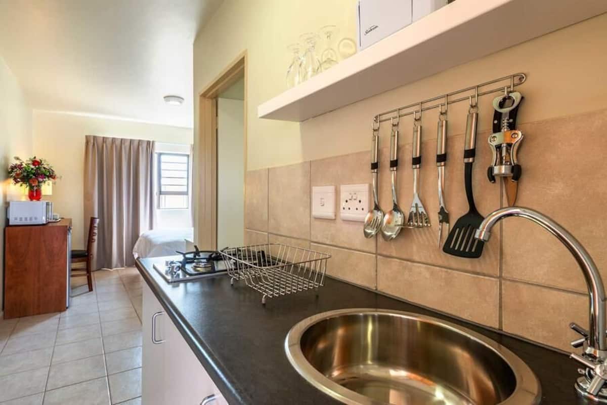 A modern kitchen with a stainless steel sink, a black countertop, and a variety of kitchen utensils hanging on the wall.
