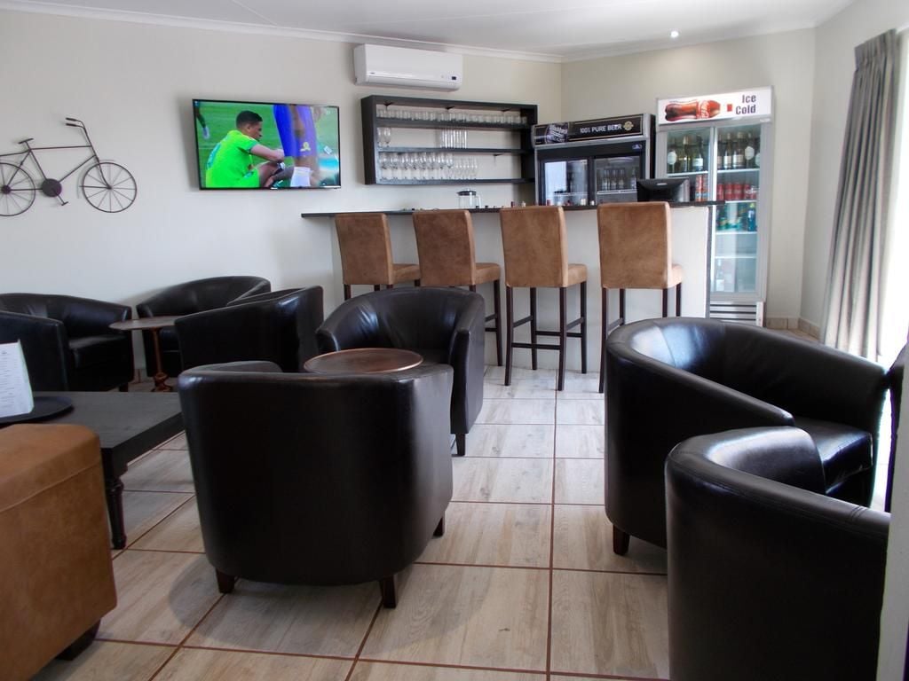 Een bar met een televisie, barstoelen en een koelkast.