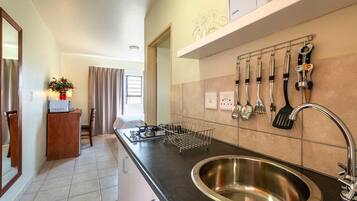 Una cocina con un lavamanos de acero inoxidable, una encimera con una cesta de alambre y un soporte de utensilios en la pared.