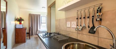 A kitchen with a stainless steel sink, a countertop with a wire basket, and a wall-mounted utensil rack.