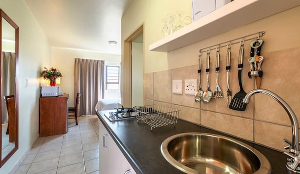 A kitchen with a stainless steel sink, a countertop with a wire basket, and a wall-mounted utensil rack.