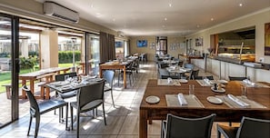 A restaurant with outdoor seating, a kitchen visible through a glass partition, and a TV mounted on the wall. - Kathu Inn (Kathu)
