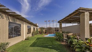 A backyard with a swimming pool, covered patio, and a small garden area. - Kathu Inn (Kathu)