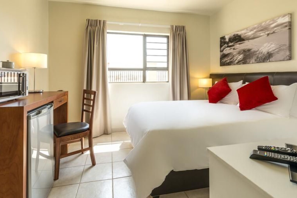 Una habitación de hotel con una cama, un escritorio con microondas, una silla y un televisor.