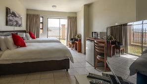 A hotel room with two beds, a desk, a chair, a TV, and a balcony with curtains. - Kathu Inn (Kathu)