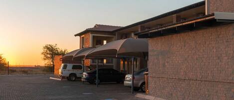 A parking area with covered carports and a building with a brick facade.