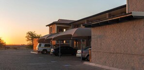 A parking area with covered carports and a building with a brick facade. - Kathu Inn (Kathu)