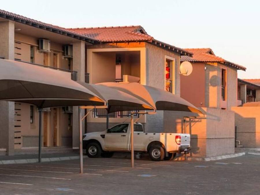 A row of hotel buildings with covered parking and a car parked in front.