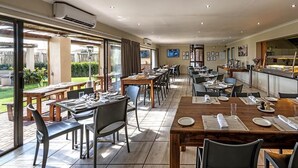 A restaurant with outdoor seating, a kitchen visible through a glass partition, and a TV mounted on the wall. - Kathu Inn (Kathu)
