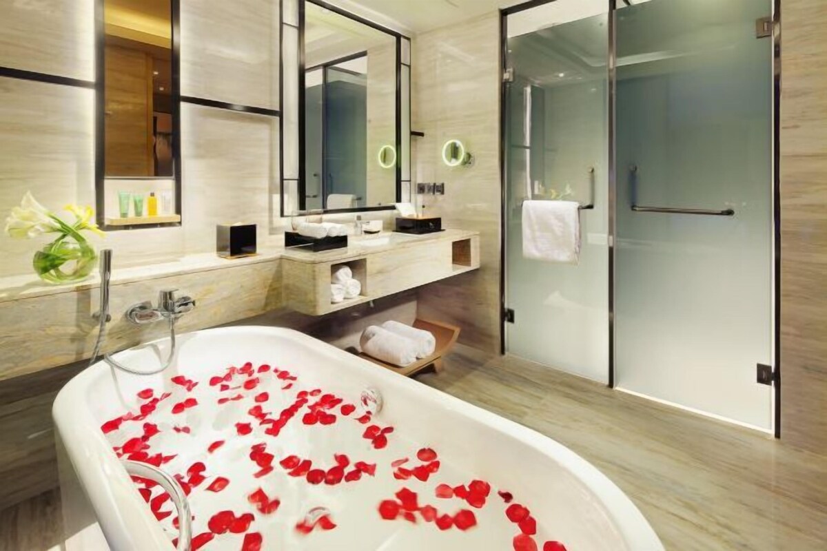 A modern bathroom with a freestanding bathtub filled with rose petals, a large mirror, and a glass shower enclosure.