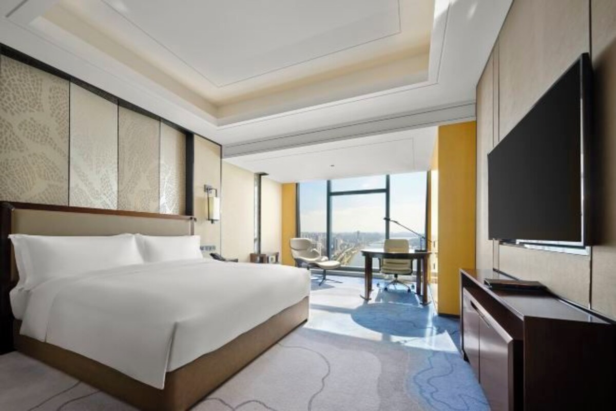 Habitación de hotel con una cama grande, un escritorio, una silla, un televisor de pantalla plana y un ventanal con vistas a la ciudad.