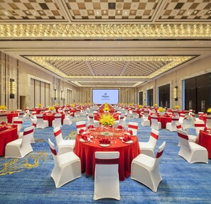 A large banquet hall with round tables, white chairs, and red tablecloths.