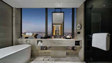 A modern bathroom with a large bathtub, a vanity with a mirror, and a view of the cityscape.
