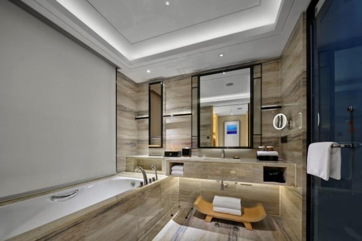 A modern bathroom with a large mirror, a bathtub, and a vanity with a towel rack.