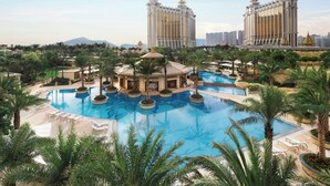 A large outdoor swimming pool surrounded by palm trees and lounge chairs, with two tall buildings in the background. - JW Marriott Hotel Macau (Cotai)