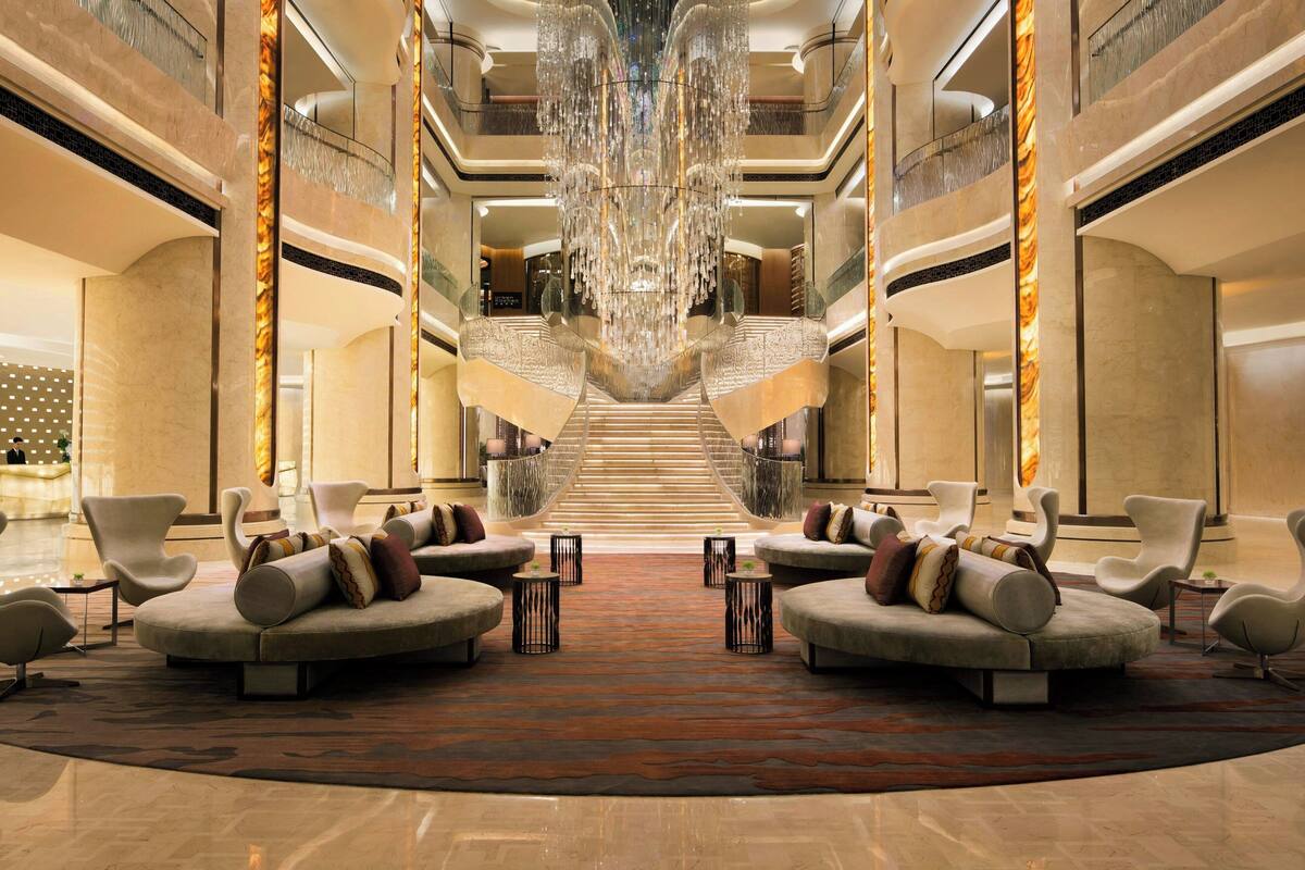 A spacious lobby with a grand chandelier, a central staircase, and modern seating areas.