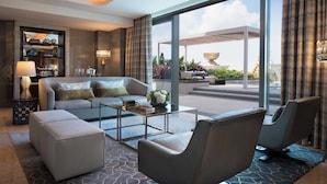 A modern hotel room with a sofa, ottoman, and chairs, a coffee table, a bookshelf, and large windows offering a view of the outdoors. - JW Marriott Hotel Macau (Cotai)