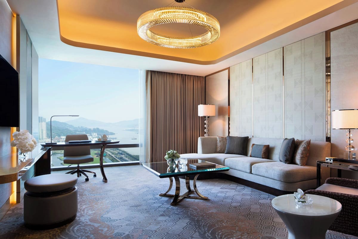 A modern hotel room with a large window, a sofa, a coffee table, and a desk with a chair.