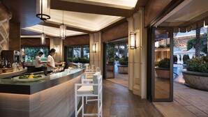A modern bar area with a counter, bar stools, and a view of an outdoor garden with palm trees and a pool. - JW Marriott Hotel Macau (Cotai)