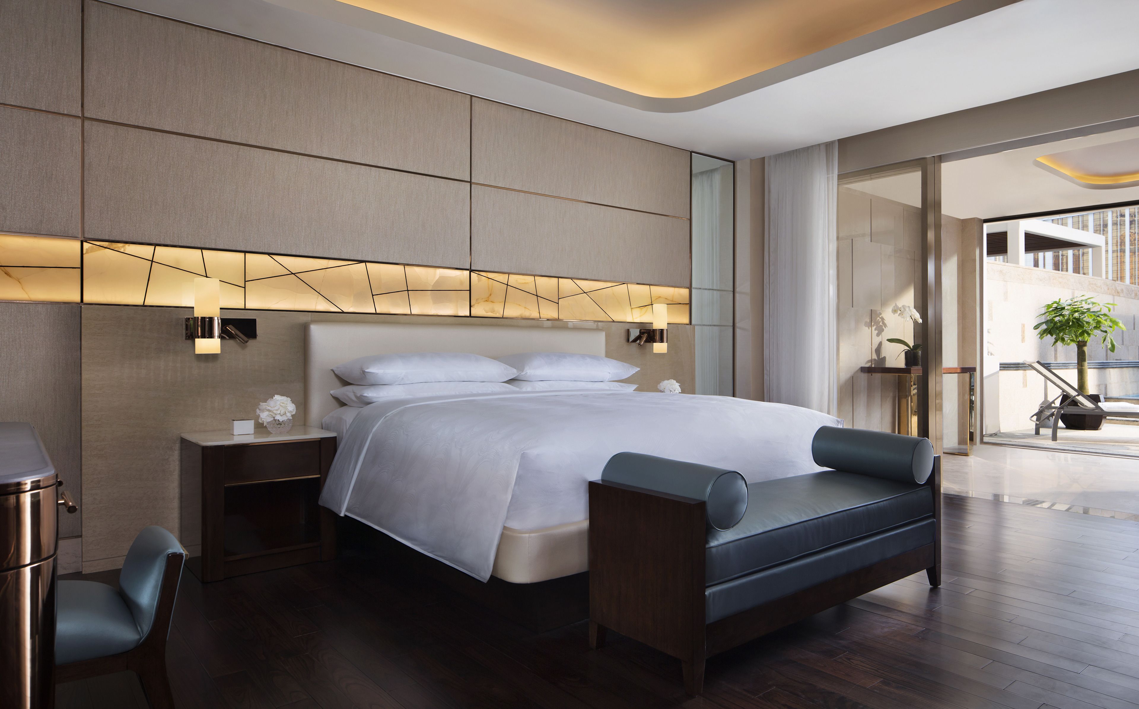 A modern hotel room with a large bed, bedside tables, a sofa, and a view of the outdoors.