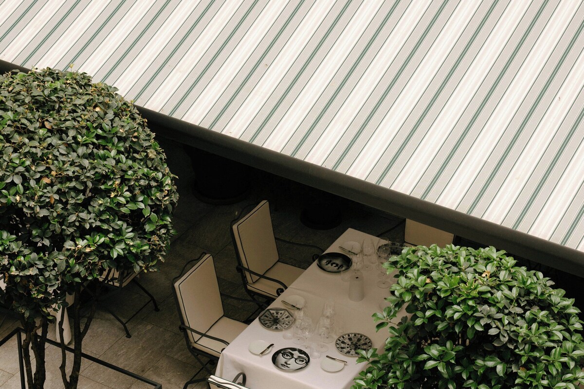 An outdoor dining area with a table set for two, surrounded by chairs, and enclosed by a metal railing.