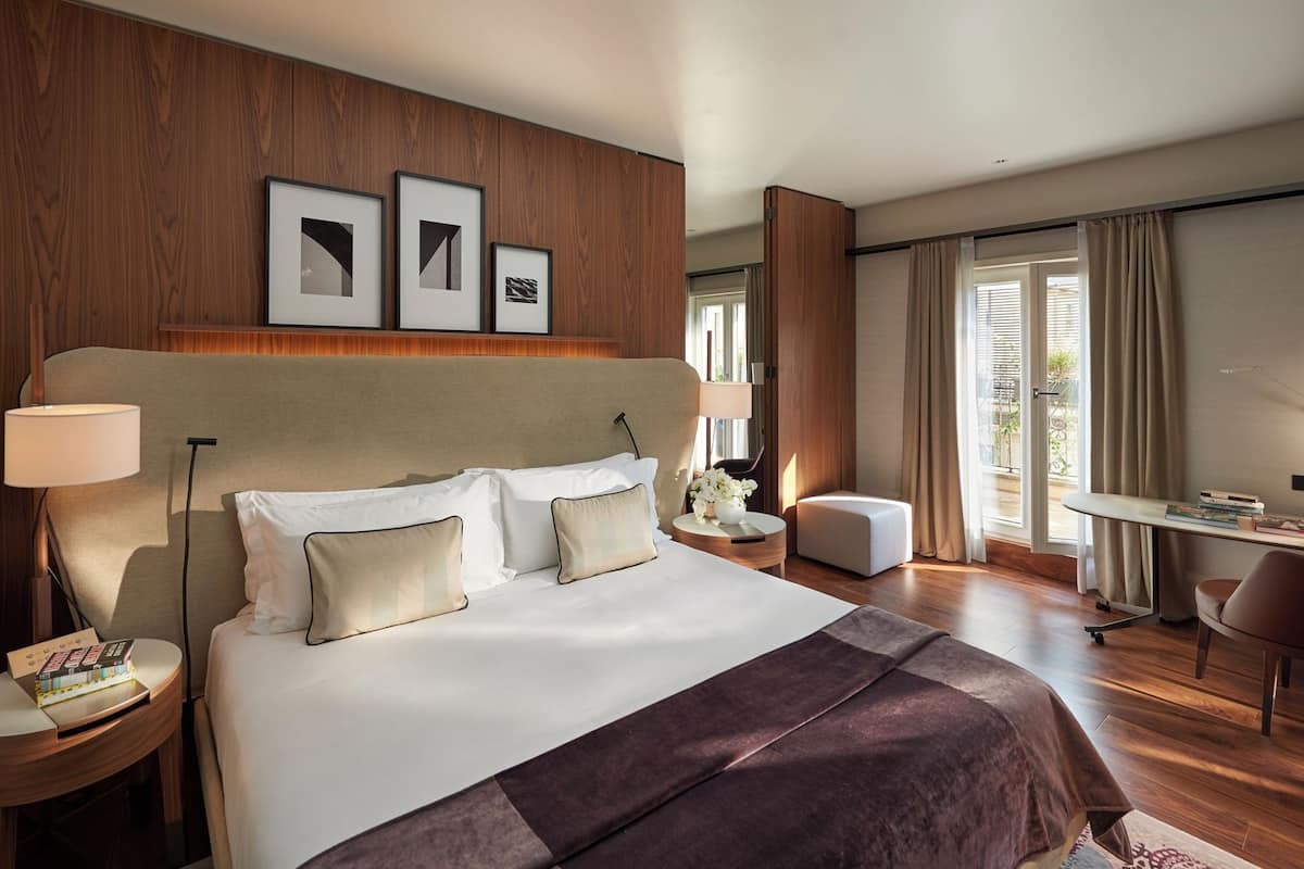 A hotel room with a large bed, bedside tables, a desk, and a view through a window.