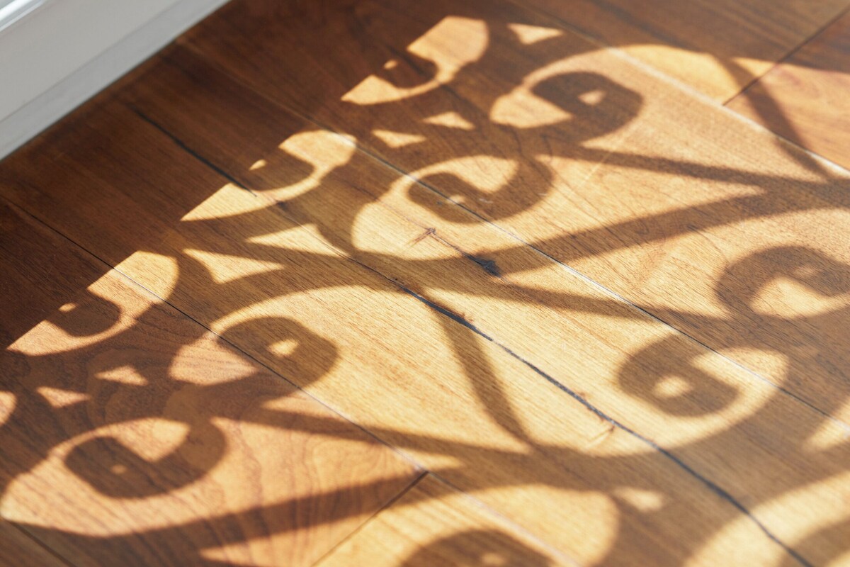 A wooden floor with intricate shadow patterns cast by a metal railing.