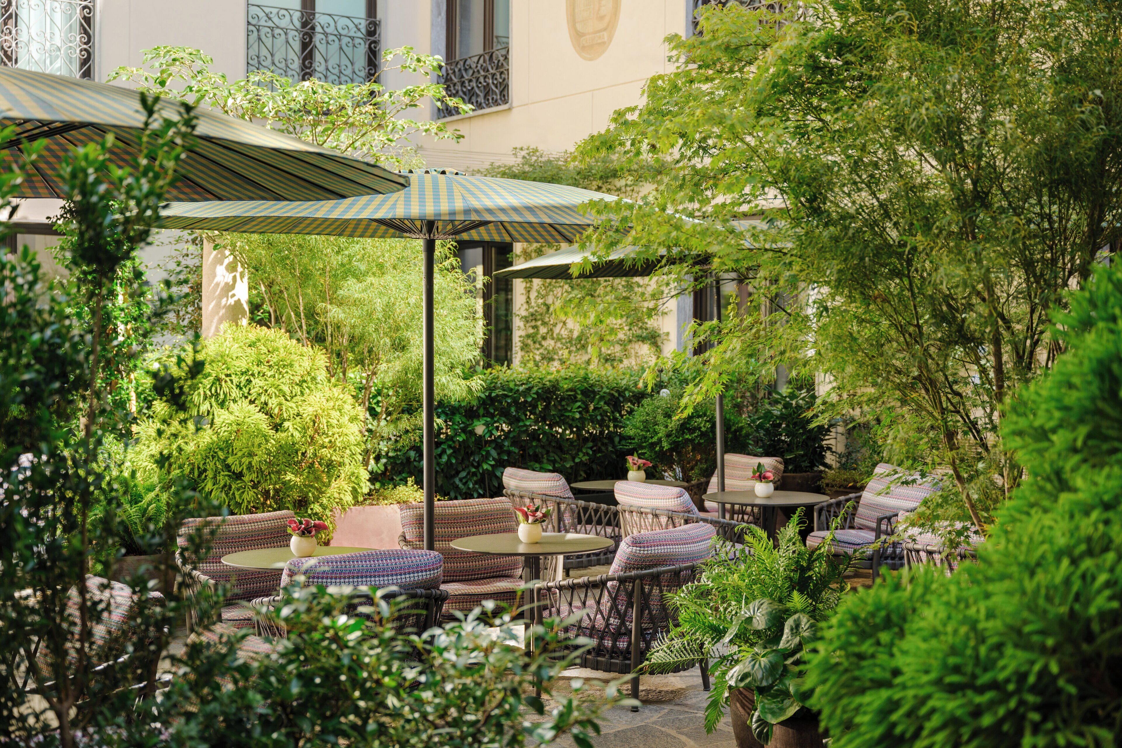 An outdoor patio area with wicker furniture, umbrellas, and lush greenery.