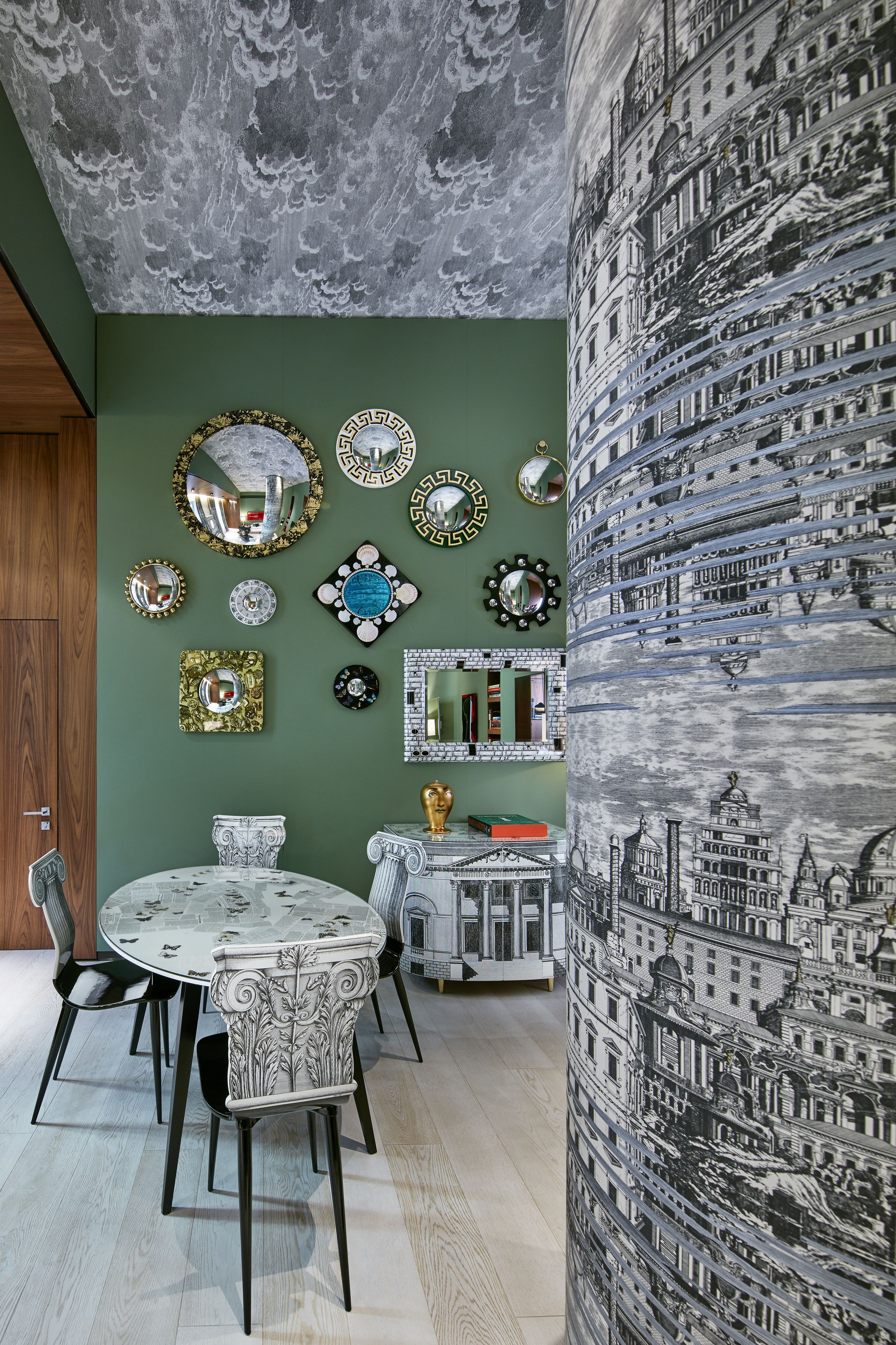 A dining area with a round table, chairs, and a wall adorned with various mirrors and decorative plates.