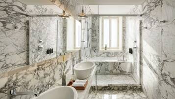 Bagno con parete in marmo, vasca freestanding, lavabo a incasso, zona doccia e illuminazione a sospensione.