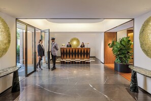 A modern lobby with a reception desk, marble flooring, and a large potted plant.