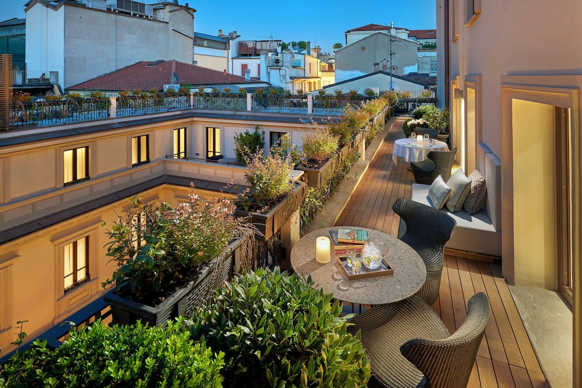 A rooftop terrace with outdoor seating, a table with drinks and books, and a view of surrounding buildings.